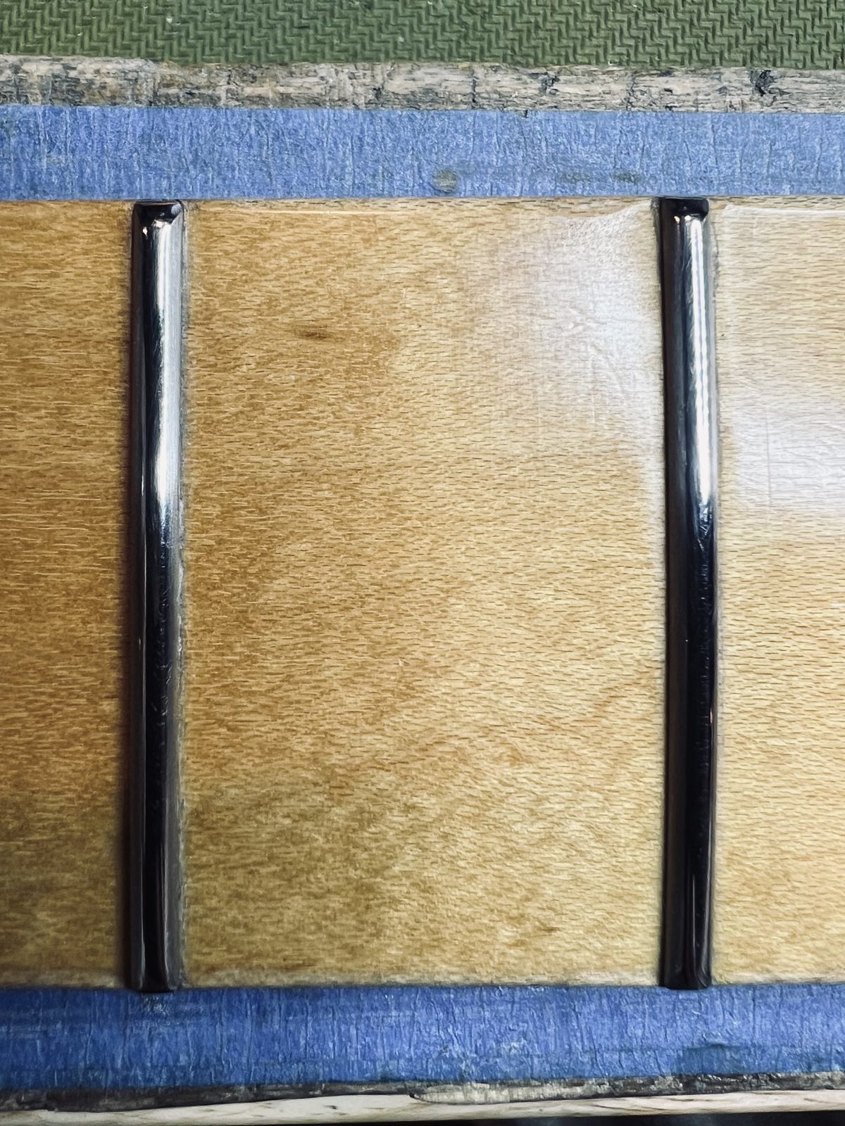 Macro detail of polished jumbo stainless frets seated into the original finish of a maple fretboard with no chipout